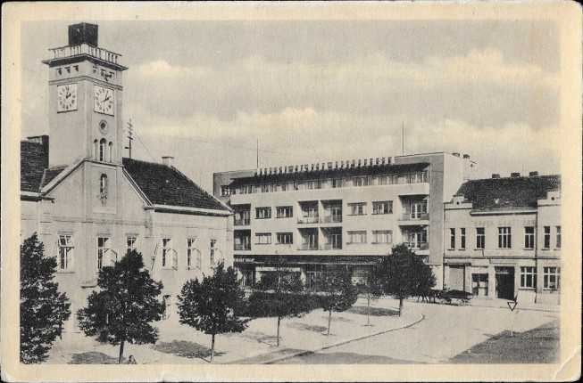Na pohlednici je budova bval radnice s vikou a hodinami, budova zlony a jet jedna men budova. Je vidt chodnky silnici a adu malch strom.