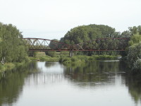 Na zbru fotografie z vletu je vidt eku travnat behy, listnat stromy a star eleznin most.