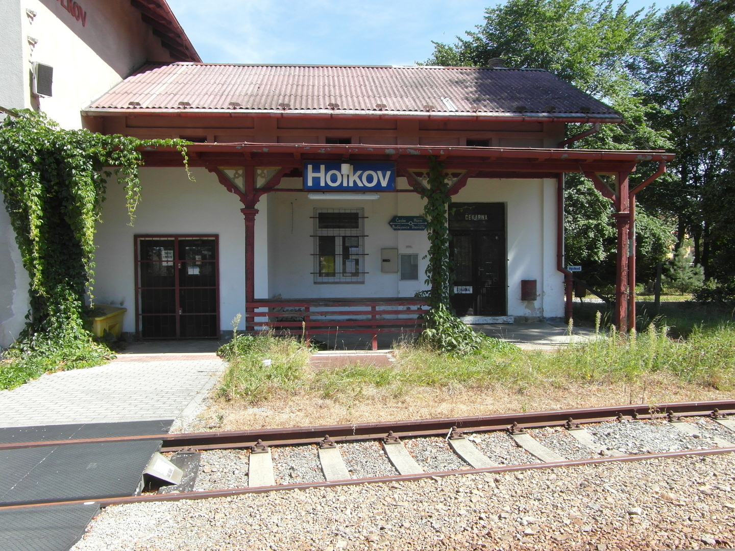 Na fotografii eleznin stanice Holkov je vidt budovu s pstekem i jedny koleje. Budova je omtnuta ed. Napravo od n je
  v pozad kousek zelen.