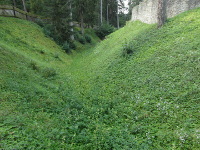 Na fotografii je vidt pkop, plot a parknov ze kolem hradu. Svahy pkopu jsou porostl rostlinami, 
  kei a stromy.