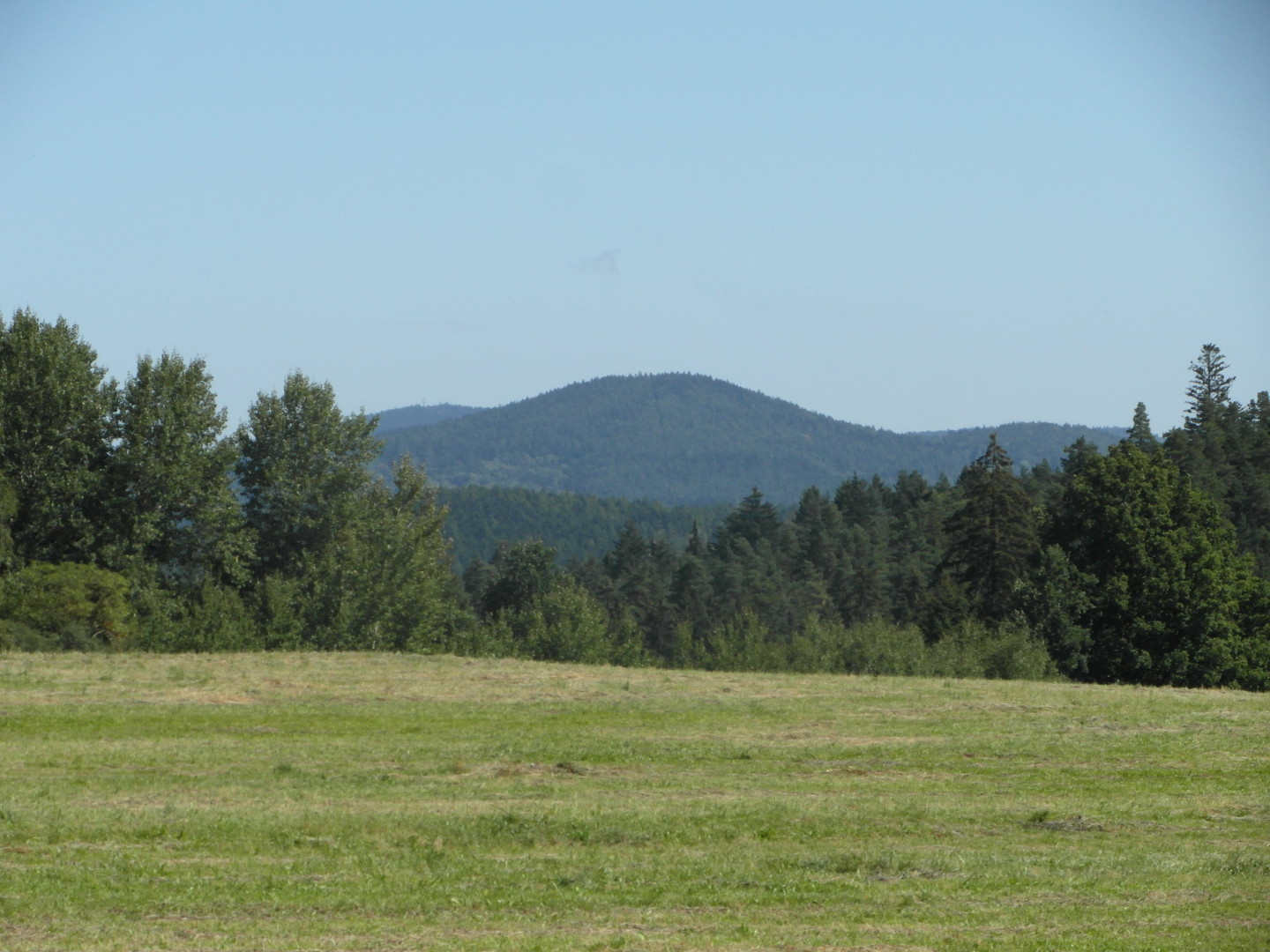 Na fotografii je vidt louka, v pozad les a hory. Hora uprosted je vysok. Ob krajn jsou v pozad. 
  Na fotografii jsou v tto velikosti jet dal dva kopce vzadu.