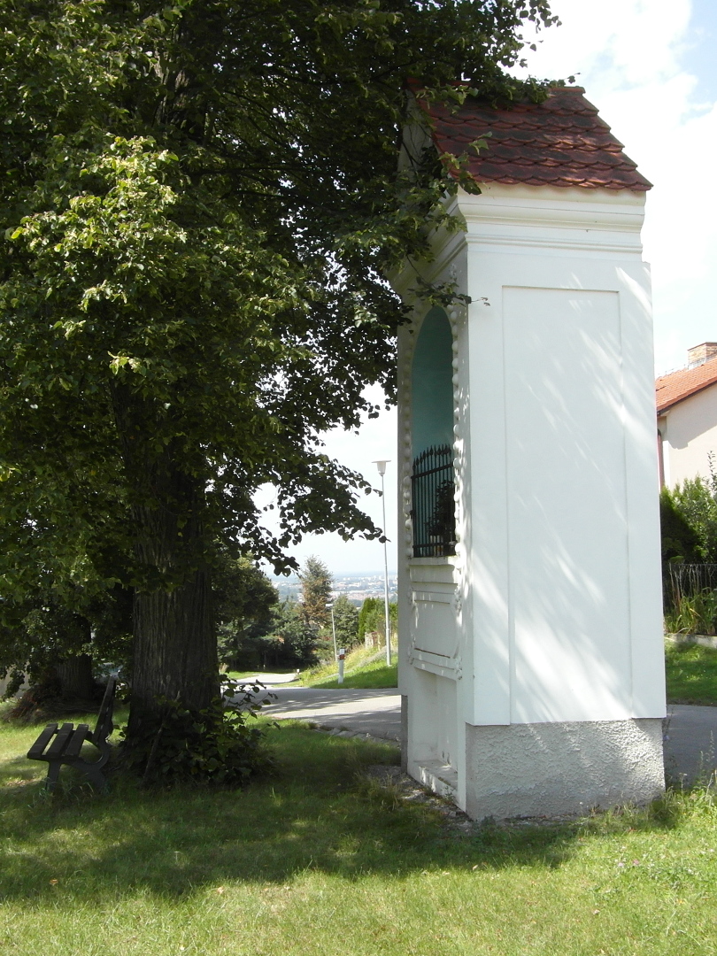 Na fotografii z vletu ble omtnut kaple s modrm vklenkem. Vedle n je lpa, kter ji
          pi fotografovn sten zakrv. Doln st vklenku je zajitn ocelovou m. Kolem je louka.
          Zbr je pozen z boku tak, e je vidt kaple skoro cel. U lpy je lavika.