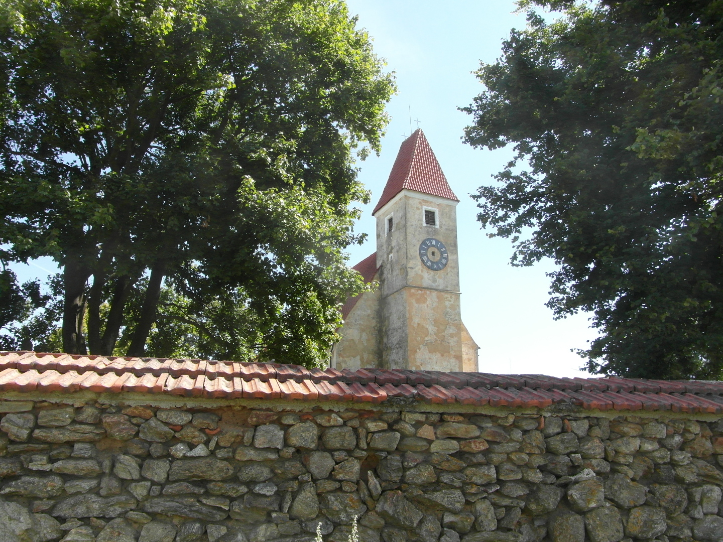 Na fotografii z vletu je 
  v kostela a kolem n mohutn stromy. Jeden z nich prakticky zakrv lo kostela. 
  Velmi opadvajc omtka m okrovou barvu. Je vidt, e vn hodiny jsou pokozen.
  Nemaj ruiky. Znanou st doln sti fotografie zabr ze hbitova. V tomto 
  mst je neomtnut, take je vidt kameny.