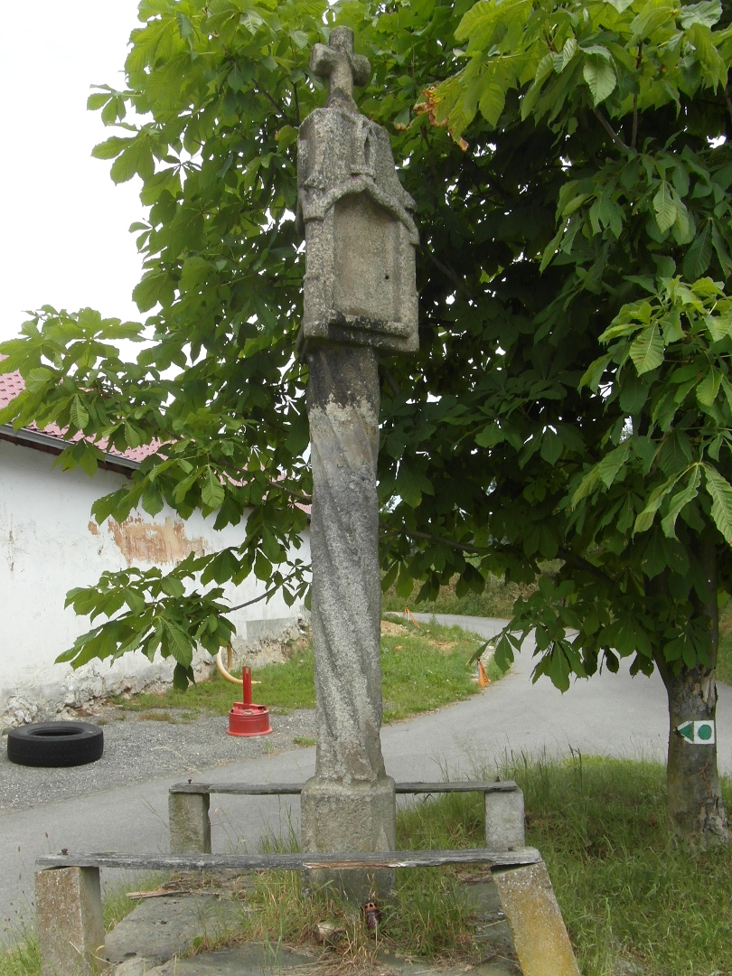 Na fotografii z vletu jsou kamenn sloupov Bo muka s ohrdkou, silnice a budova. 
  Hlavice Boch muk je ozdobn a je umstna na korintskm sloupu. Na hlavici je kamenn
  kek.